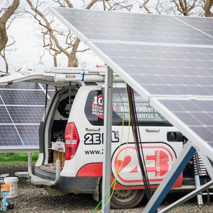Photo of a 2E Electrical van parked between 2 rows of solar panels