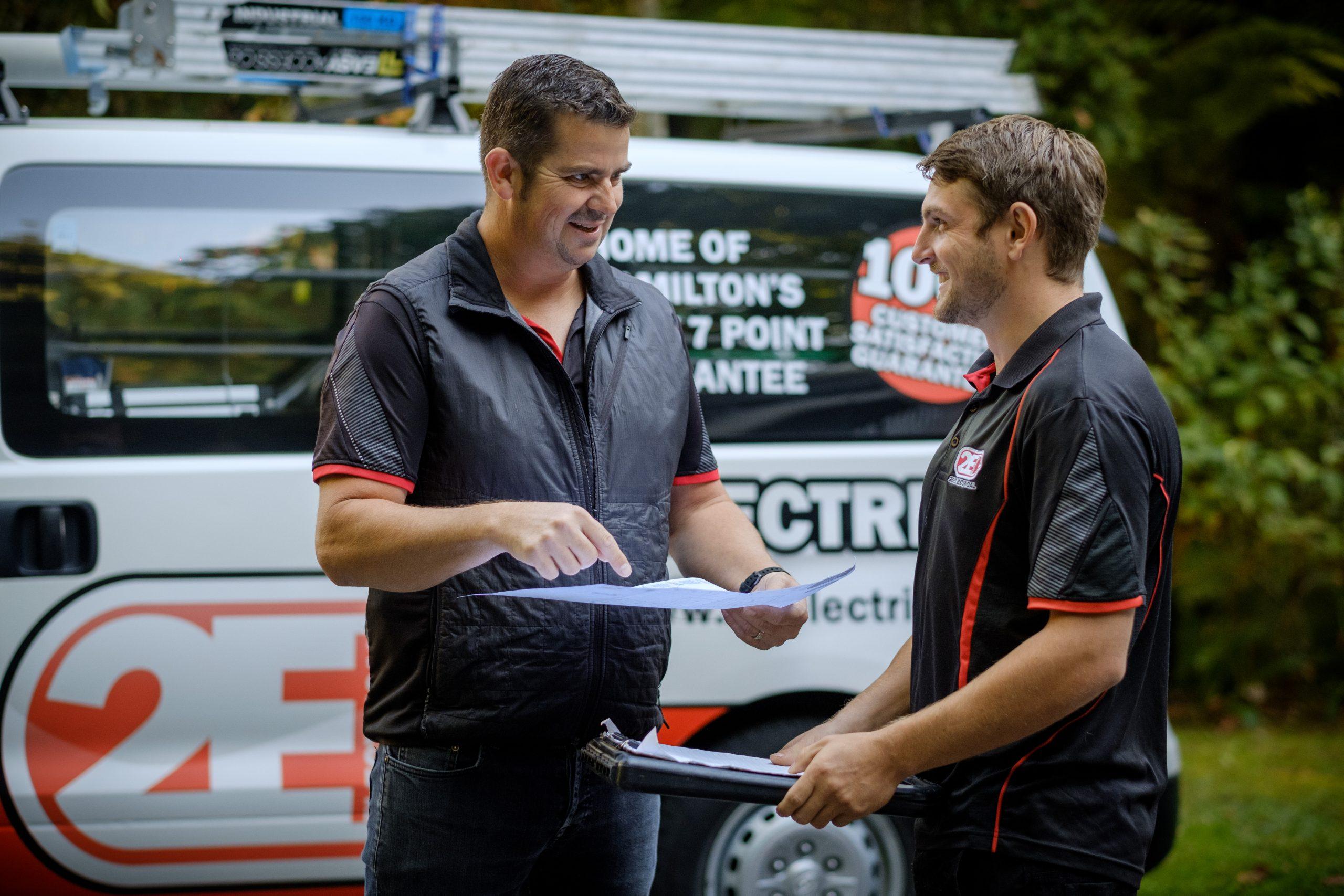 Two 2E Electrical team members reviewing documents beside a branded service van