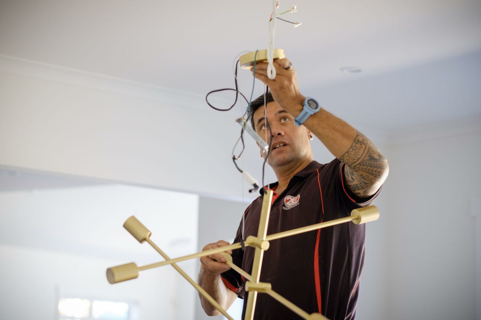 Electricians from 2E Electrical installing a modern gold pendant light fixture in a bright residential living space.