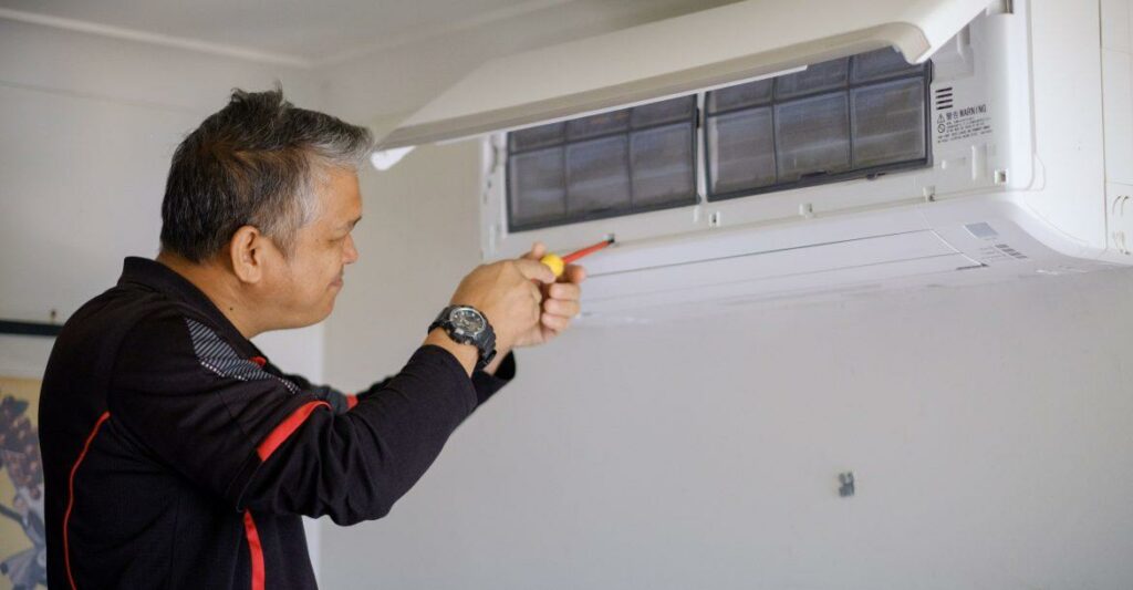 Electrician in uniform servicing a wall-mounted heat pump unit using a screwdriver